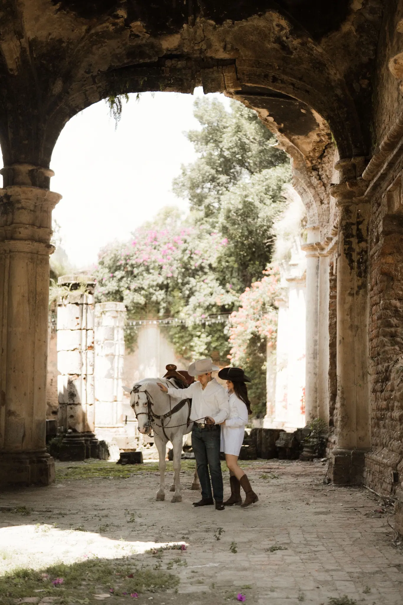 Nathalia y Rubén junto a un caballo bajo un arco de hacienda